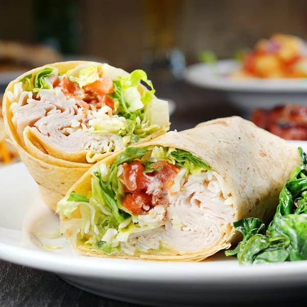 Two halves of a chicken wrap with lettuce, tomato, and sauce, served with a side of spinach.