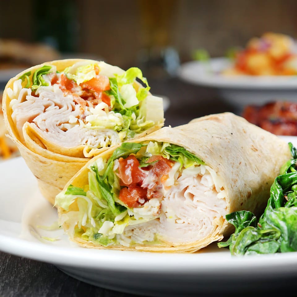 Two halves of a chicken wrap with lettuce, tomato, and sauce, served with a side of spinach.
