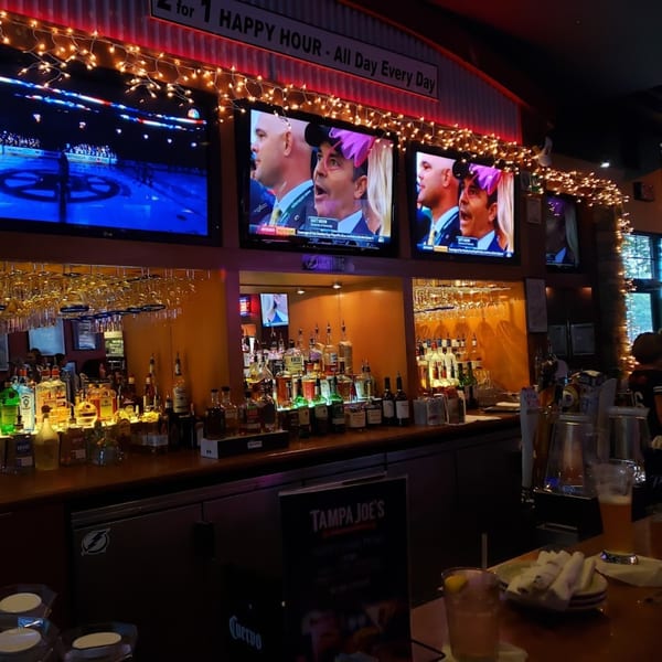 A sports bar interior with multiple TVs showing sports, a fully stocked bar, and string lights.