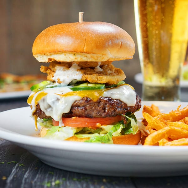 A Tampa Joe's burger with melted cheese, jalapenos, and onion rings, served with fries and beer.