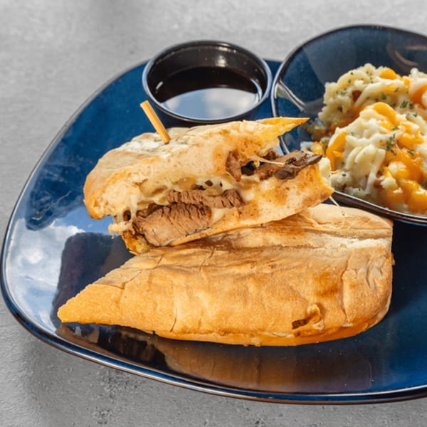 Tampa Joe's Philly cheesesteak sandwich with a side of mac and cheese and dipping sauce.