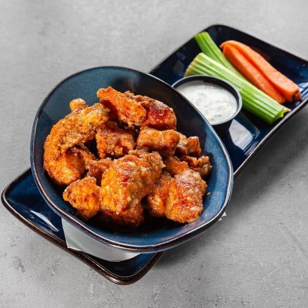 Tampa Joe's boneless wings in a blue bowl with ranch, celery, and carrots on a gray table.