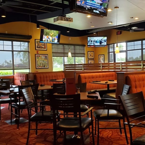 Interior of Tampa Joe's Sports Bar with orange booths, tables, chairs, and multiple TVs showing sports.